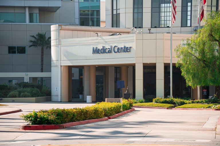 The exterior of a contemporary medical center features a prominent sign, architectural columns, and lush green landscaping