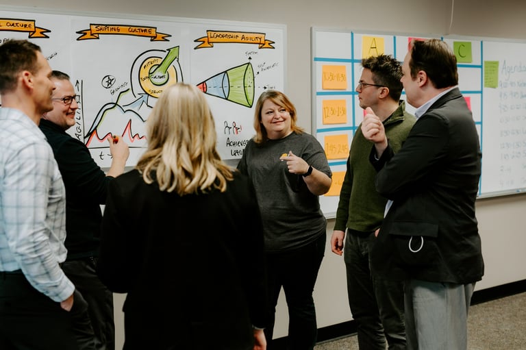 Group of six people collaborating around a whiteboard with sketches and sticky notes during a brainstorming session