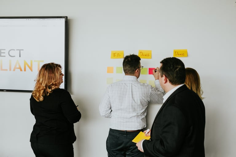 Four business professionals reviewing sticky notes on a wall during a collaborative planning session